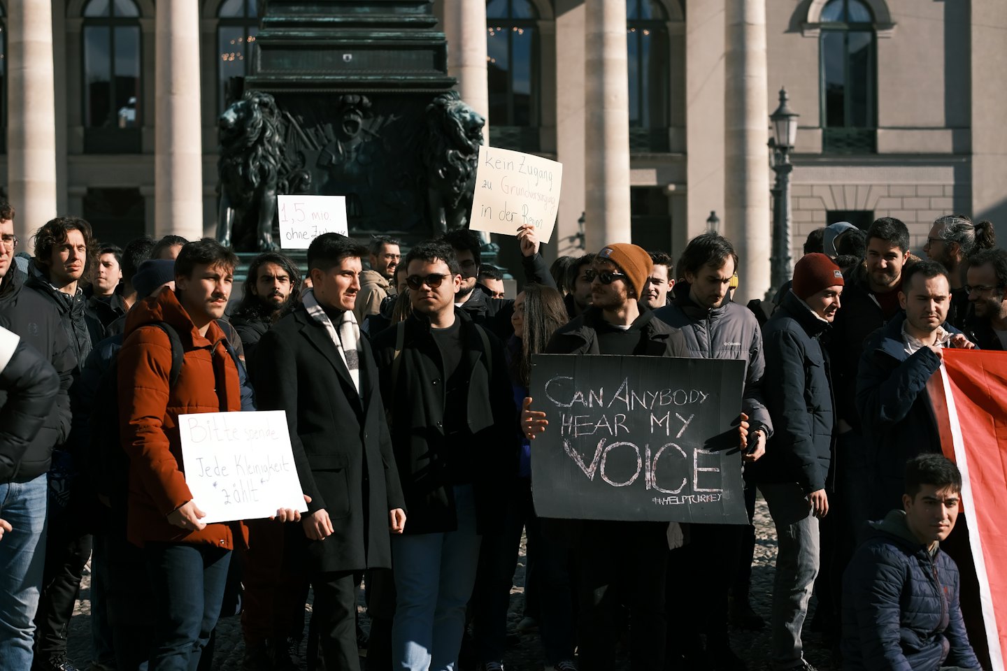 Eine Gruppe von Demonstranten mit Schildern vor einem Steingebäude.