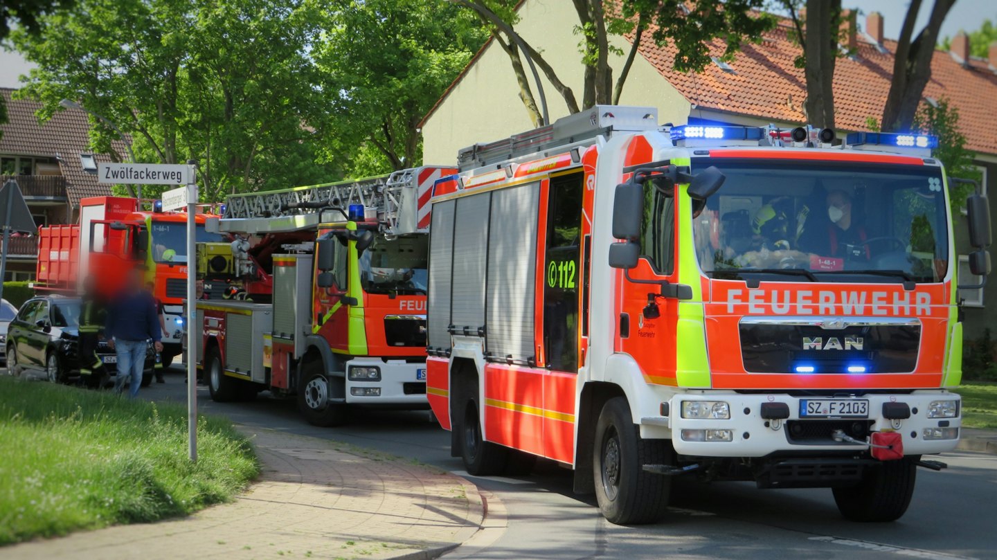 Deutsche Feuerwehrfahrzeuge parken in einer Wohnstraße mit Besatzungsmitgliedern im Inneren.